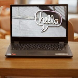 Laptop displaying 'hello' alongside iced coffee on a table in a cafe with blurred background.